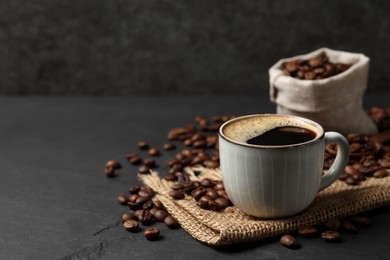 Photo of Cup of aromatic coffee and beans on black table. Space for text