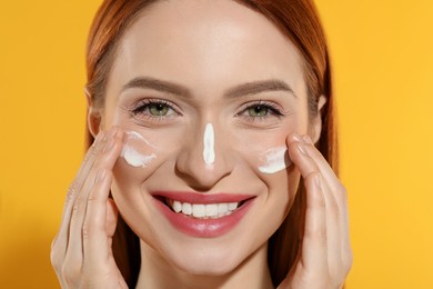 Photo of Beautiful young woman with sun protection cream on her face against orange background, closeup