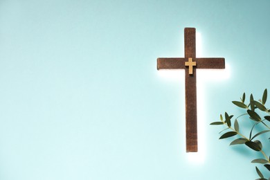Photo of Shining cross and eucalyptus branches on turquoise background, space for text. Religion of Christianity