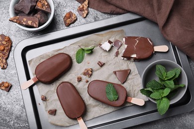 Flat lay composition with glazed ice cream bars, fresh mint and chocolate on grey table