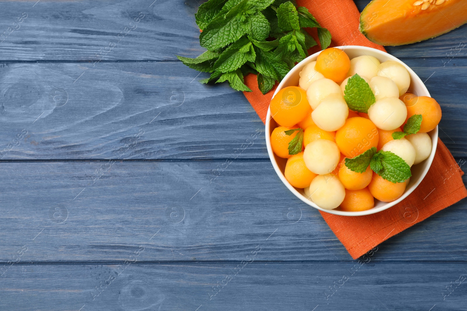 Photo of Melon balls and mint in bowl on blue wooden table, flat lay. Space for text