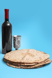Photo of Tasty matzos, wine and goblet on light blue background, space for text. Passover (Pesach) celebration