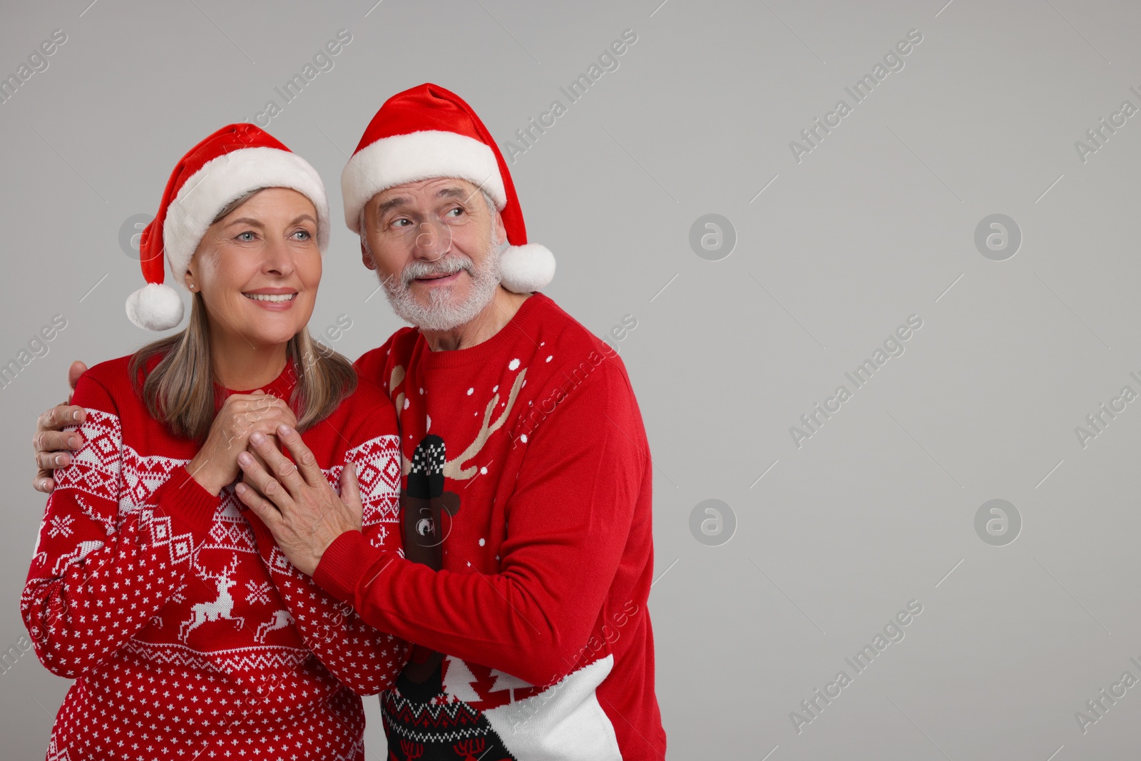 Photo of Happy senior couple in Christmas sweaters and Santa hats on grey background. Space for text