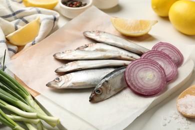 Photo of Fresh raw sprats, cut lemon and onion on white table, closeup