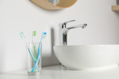 Plastic toothbrushes in glass holder on white countertop in bathroom