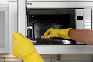 Photo of Man cleaning microwave oven in kitchen, closeup