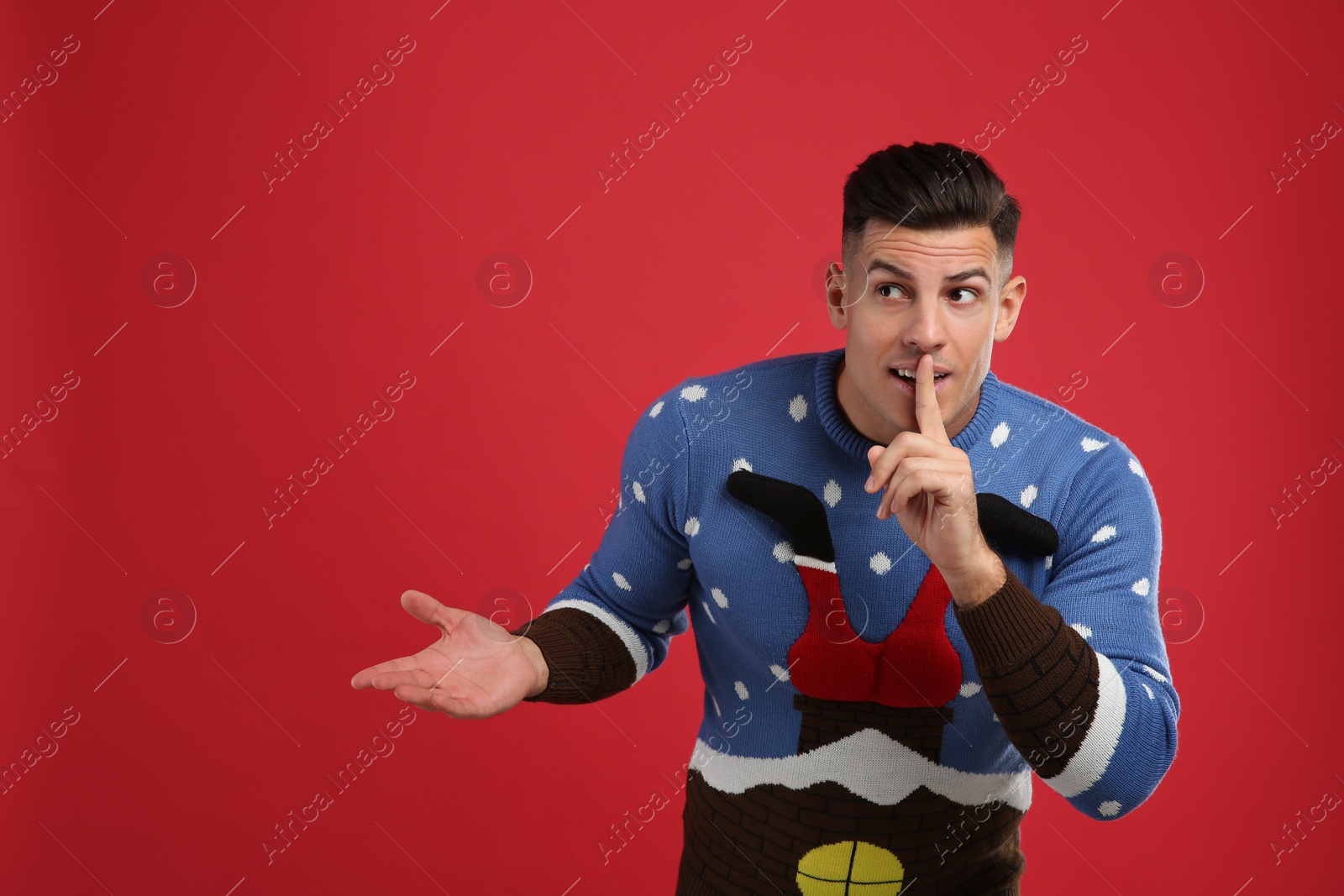 Photo of Man in Christmas sweater showing silence gesture on red background, space for text