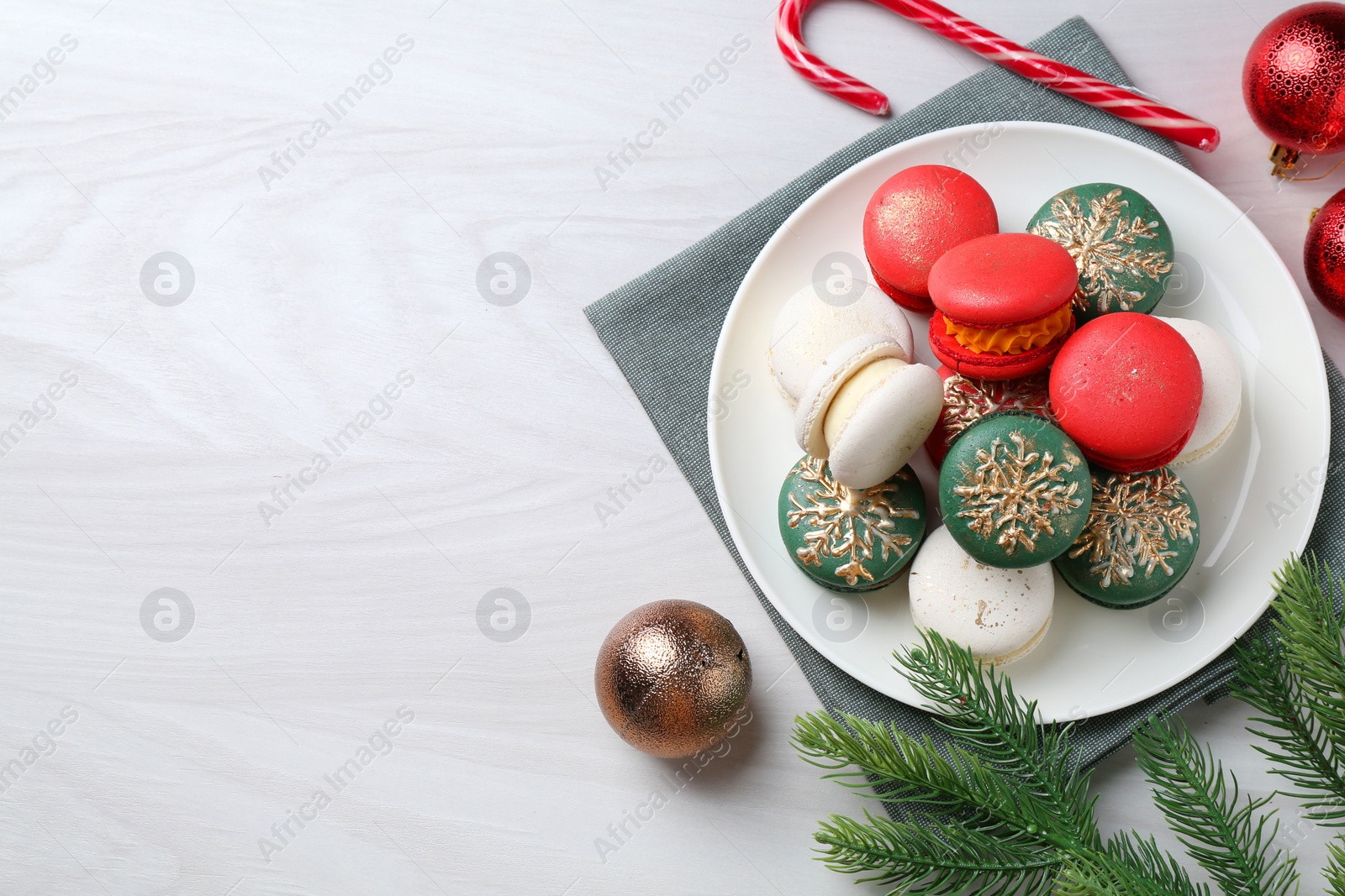 Photo of Different decorated Christmas macarons and festive decor on white wooden table, flat lay. Space for text