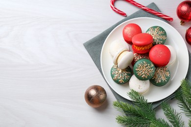 Different decorated Christmas macarons and festive decor on white wooden table, flat lay. Space for text