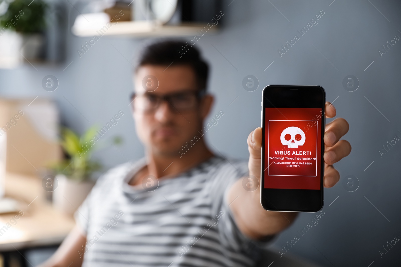 Photo of Man holding smartphone with warning about virus attack at home, focus on hand