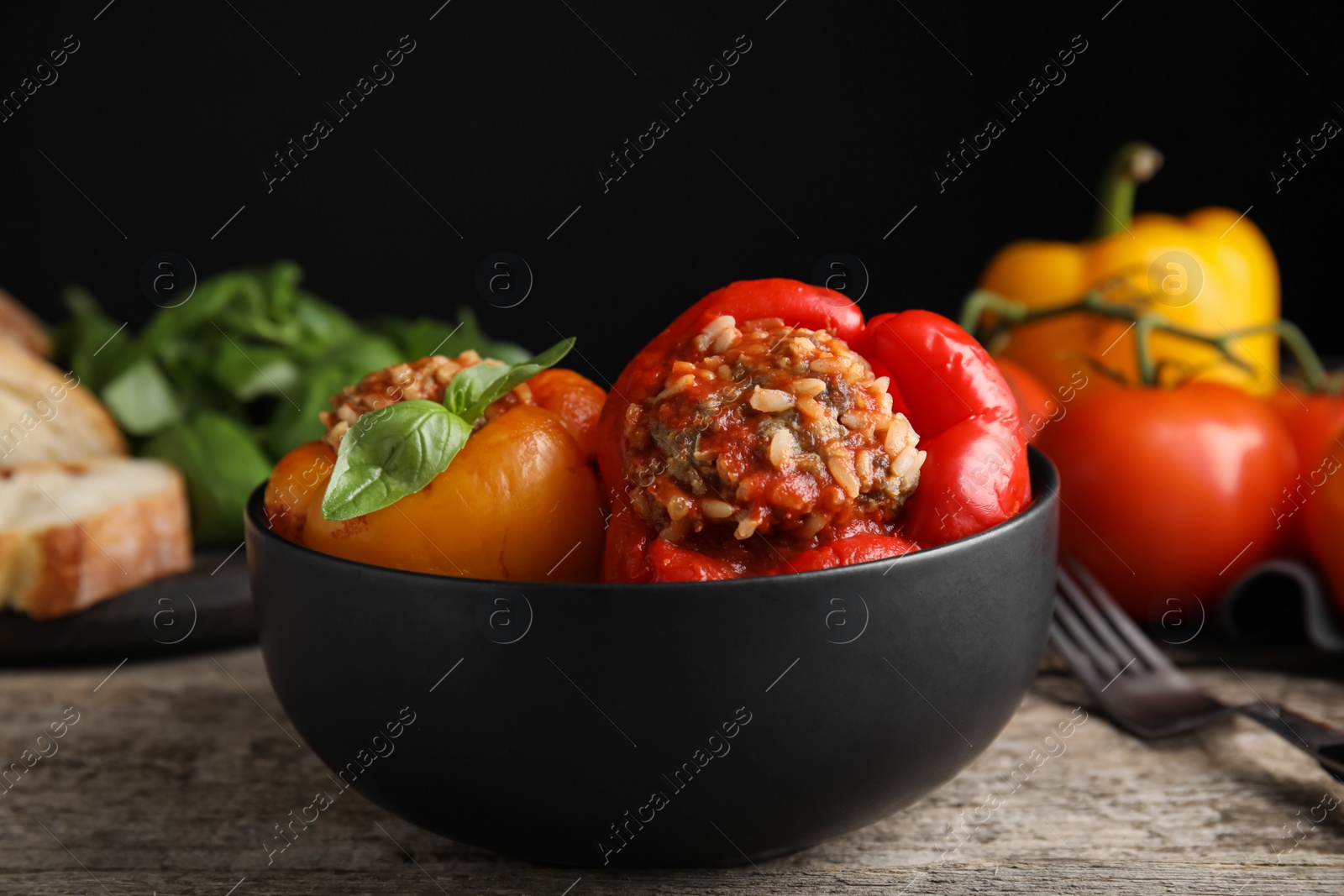 Photo of Delicious stuffed peppers with basil in bowl on wooden table