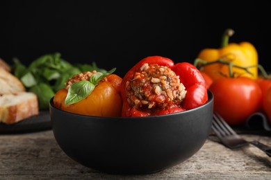 Photo of Delicious stuffed peppers with basil in bowl on wooden table