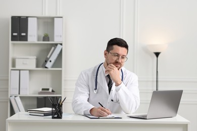 Doctor having online consultation via laptop at table in clinic