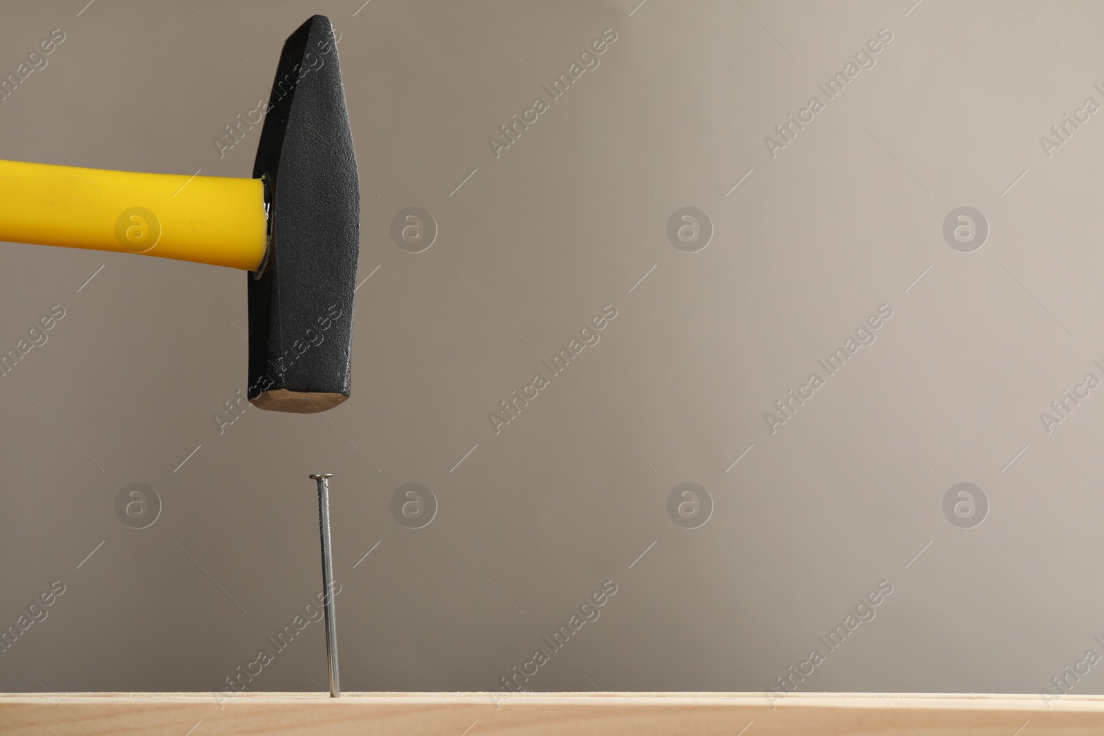 Photo of Hammering metal nail on wooden table against grey background. Space for text