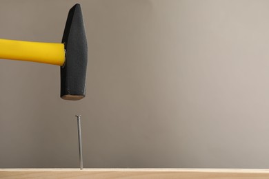 Photo of Hammering metal nail on wooden table against grey background. Space for text