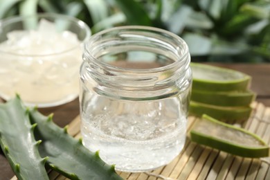 Aloe vera gel in jar and slices of plant on bamboo mat, closeup