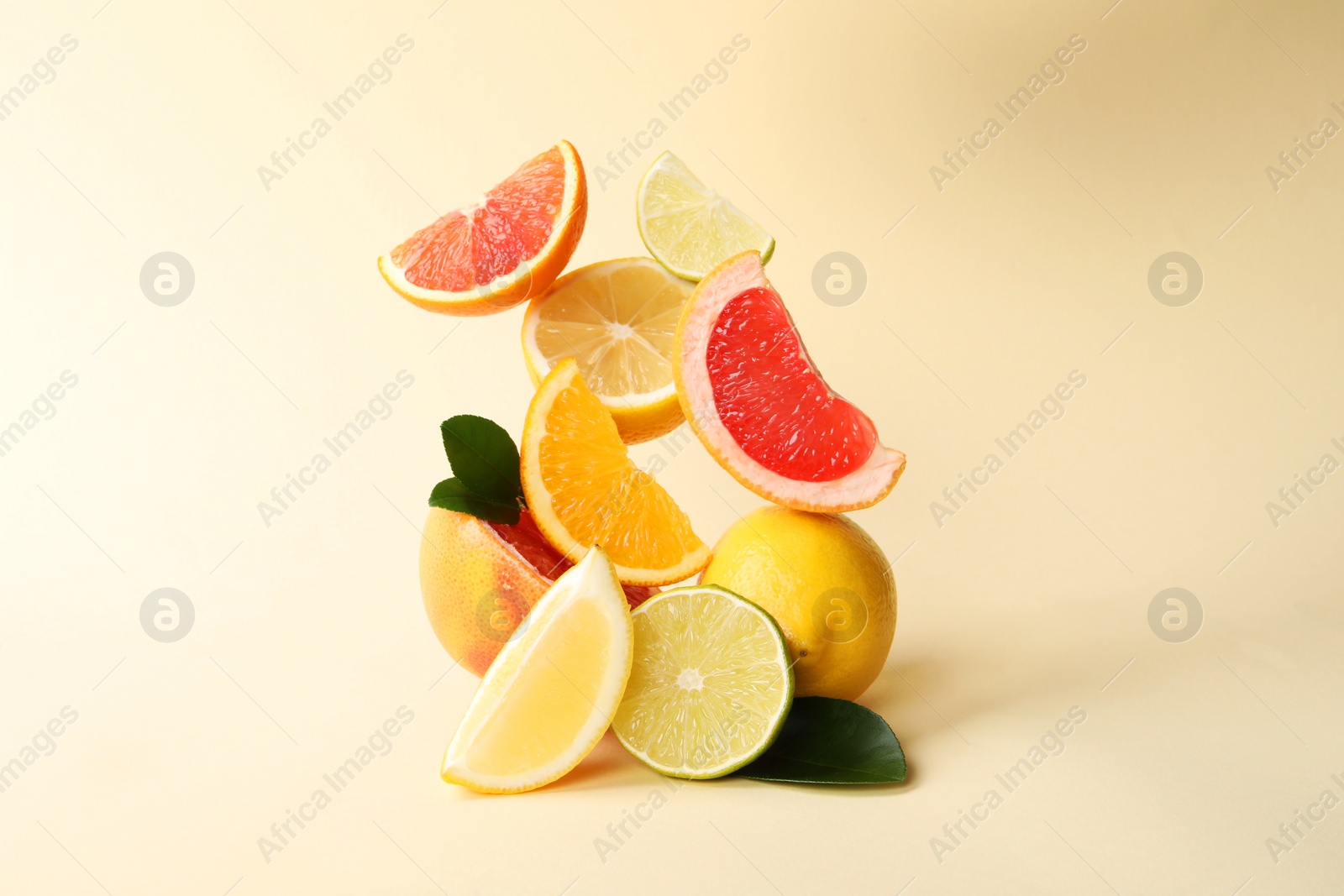 Photo of Fresh ripe citrus fruits and green leaves on beige background