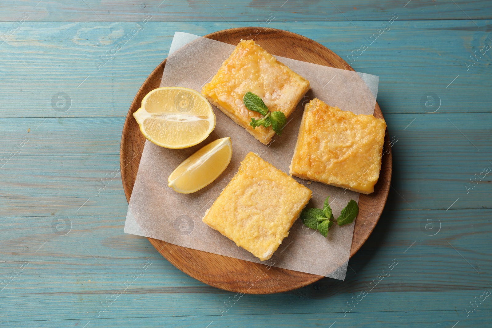 Photo of Tasty lemon bars and mint on light blue wooden table, top view