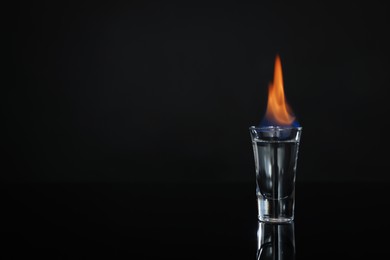 Photo of Flaming vodka in shot glass on black background, space for text
