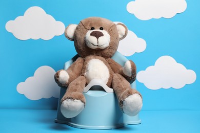 Photo of Teddy bear on baby potty against light blue background with paper clouds. Toilet training