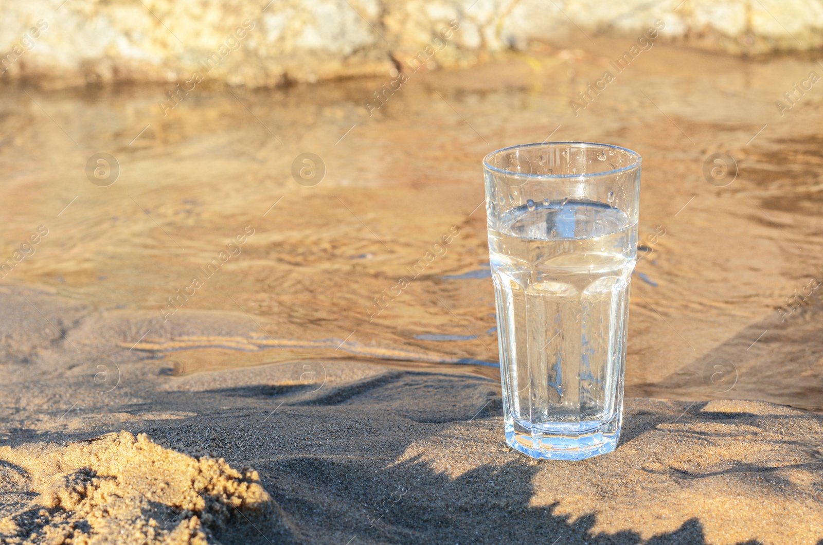 Photo of Glass of clean water on wet sand outdoors. Space for text