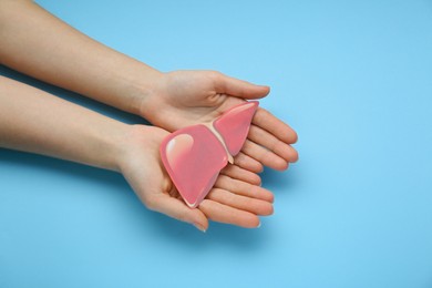 Photo of Woman holding paper liver on light blue background, closeup and top view. Hepatitis treatment