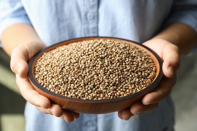 Photo of Woman holding bowl with organic hemp seeds, closeup