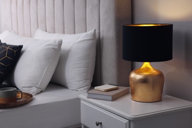 Photo of Stylish lamp and book on bedside table indoors. Bedroom interior element