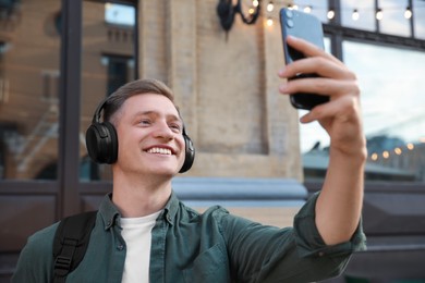 Photo of Smiling man in headphones taking selfie outdoors