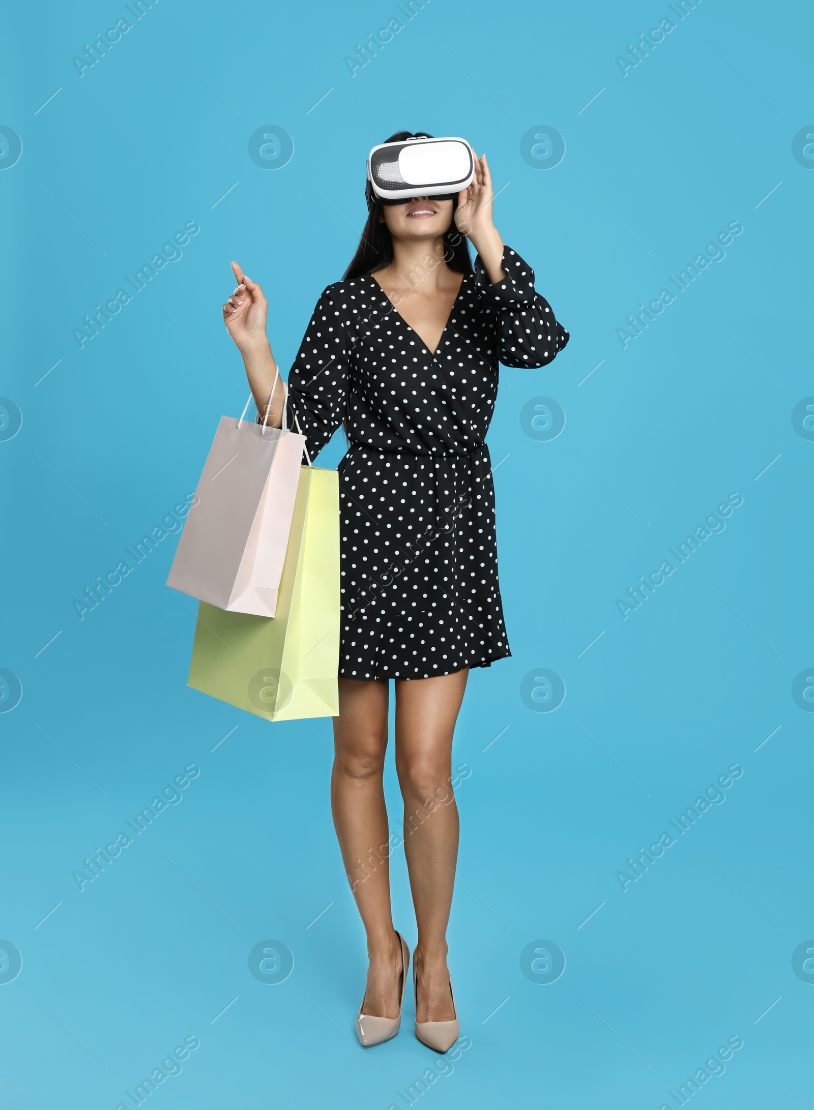 Photo of Woman with shopping bags using virtual reality headset on light blue background