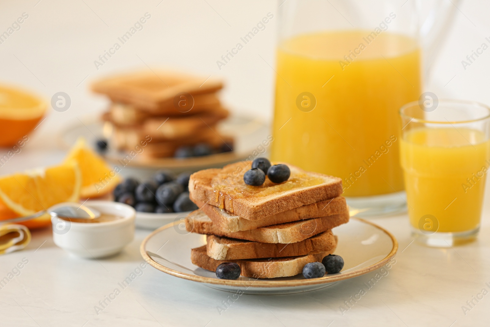 Photo of Toasted bread with jam and fresh blueberries on white table in kitchen