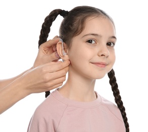 Young woman putting hearing aid in little girl's ear on white background