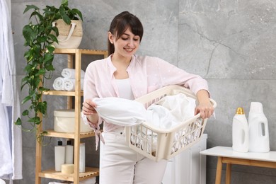 Photo of Happy young housewife holding basket with laundry in bathroom