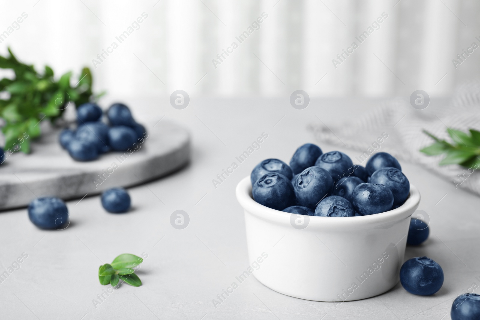 Photo of Bowl of tasty blueberries on grey table, space for text