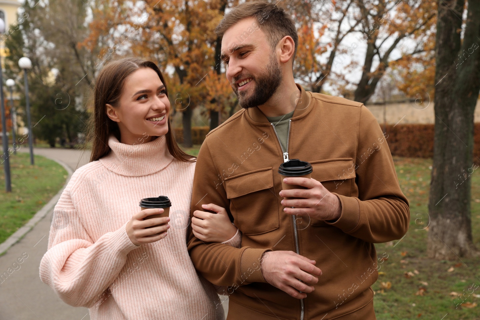 Photo of Happy couple wearing stylish clothes with cups of coffee in autumn park