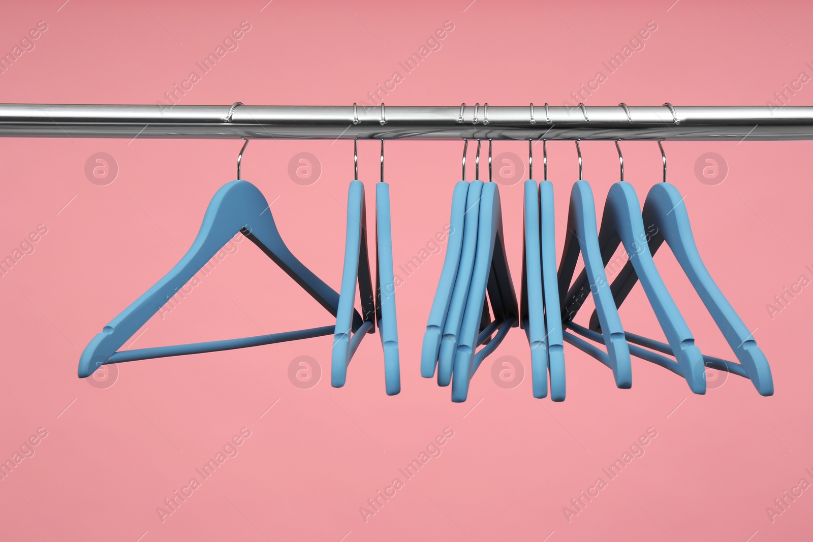 Photo of Empty clothes hangers on metal rail against color background