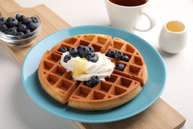 Photo of Tasty Belgian waffle with blueberries, honey and whipped cream on white table, closeup