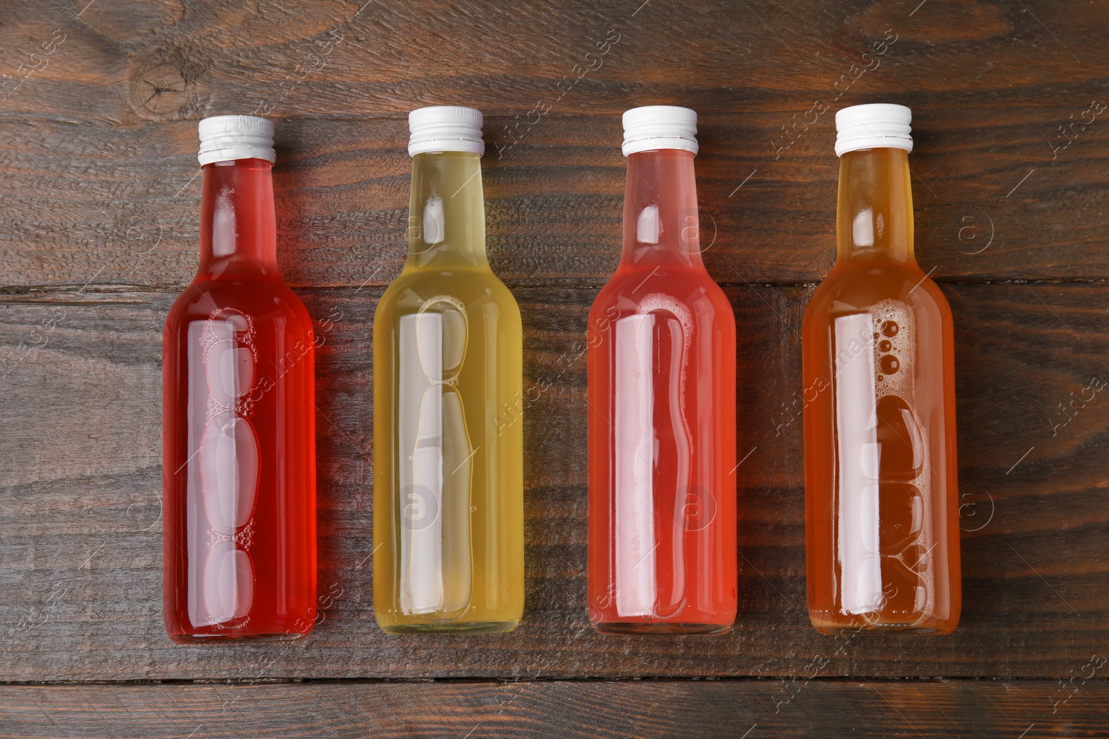 Photo of Delicious kombucha in glass bottles on wooden table, flat lay