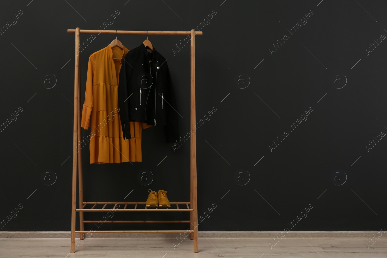 Photo of Rack with stylish clothes near black wall. Space for text