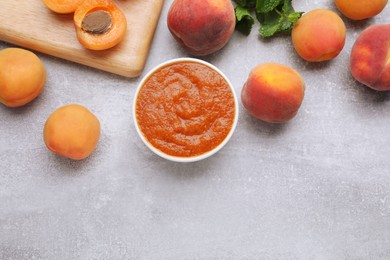 Apricot puree in bowl and fresh fruits on light grey table, flat lay. Space for text
