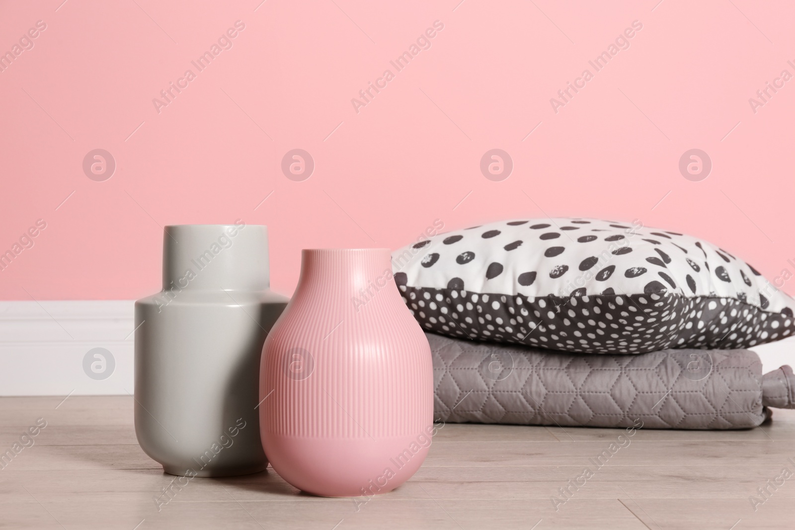 Photo of Beautiful ceramic vases with pillows for interior decoration on floor near color wall