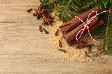 Different spices and fir branches on wooden table, flat lay. Space for text