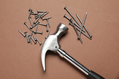 Hammer and metal nails on brown background, top view