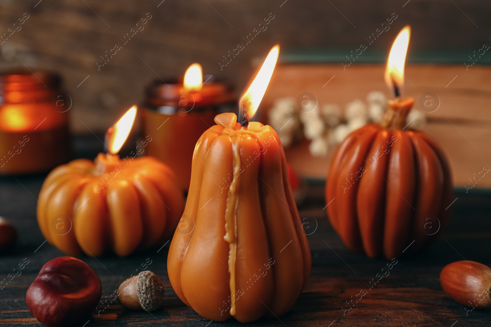 Photo of Burning candles in shape of pumpkins on wooden table, closeup. Autumn atmosphere