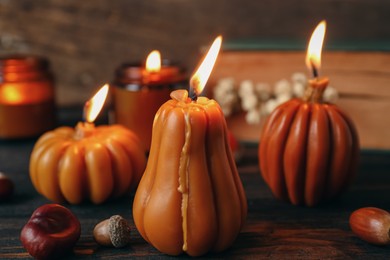 Burning candles in shape of pumpkins on wooden table, closeup. Autumn atmosphere