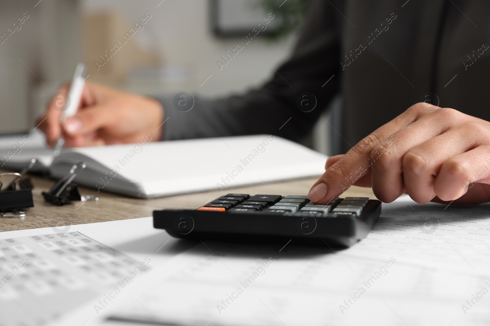 Photo of Woman using calculator while taking notes at table, closeup