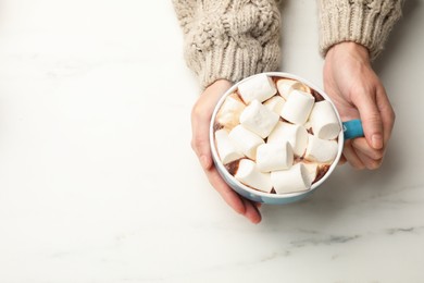 Photo of Woman with cup of tasty hot chocolate and marshmallows at white marble table, top view. Space for text