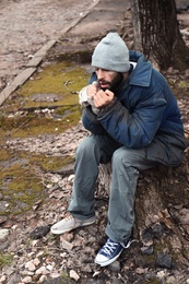 Poor homeless man sitting on stump outdoors