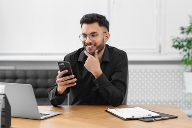 Photo of Handsome young man using smartphone at wooden table in office