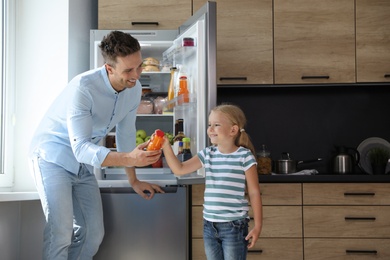 Father and daughter with bottle of juice near refrigerator in kitchen